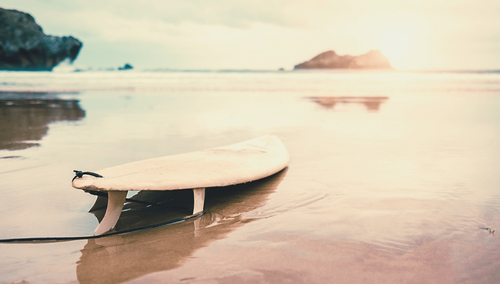 Surfboard on sandy beach at sunset