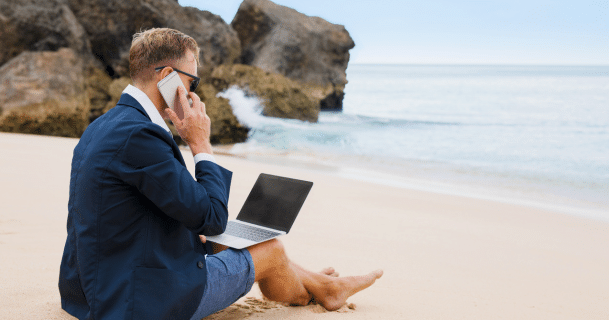 Businessman working on laptop and phone while sitting on beach